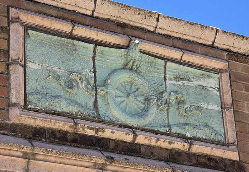 Decorative tiles depicting a wheel, snake and eagle above the doors of the repair building